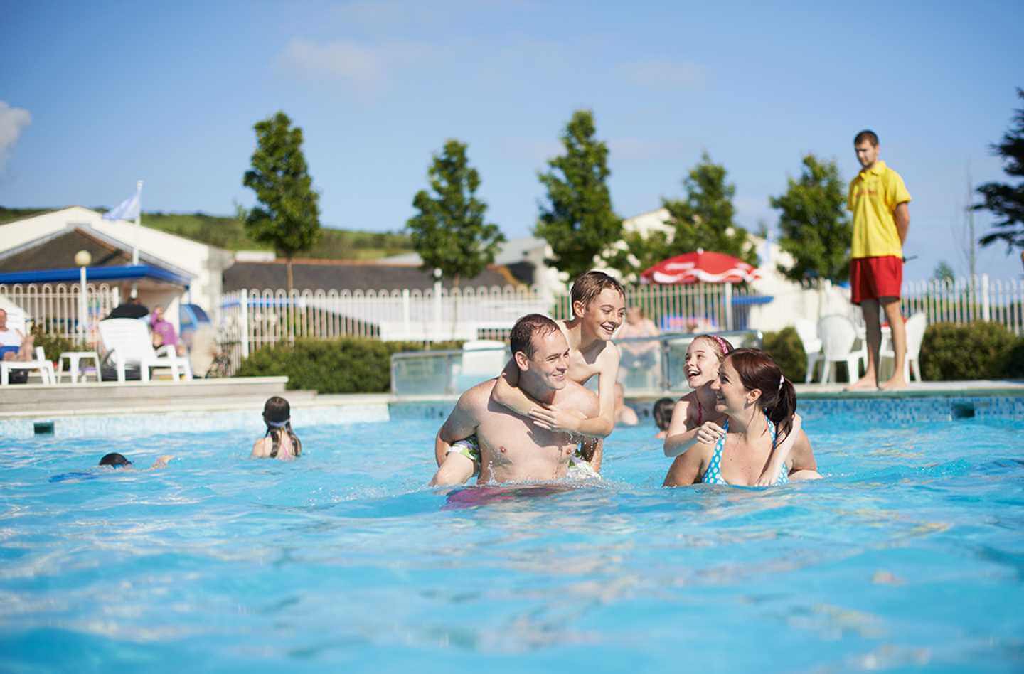 A family of four spending time together laughing in an outdoor pool