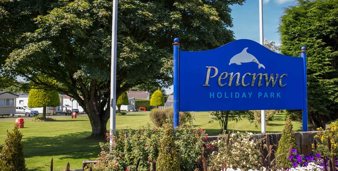 image of a sign for 'Pencnwc holiday park' with caravans in the background