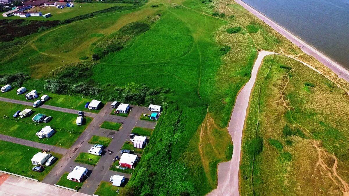 Birds-eye-view of a caravan park surrounded by greenery and next to a beach