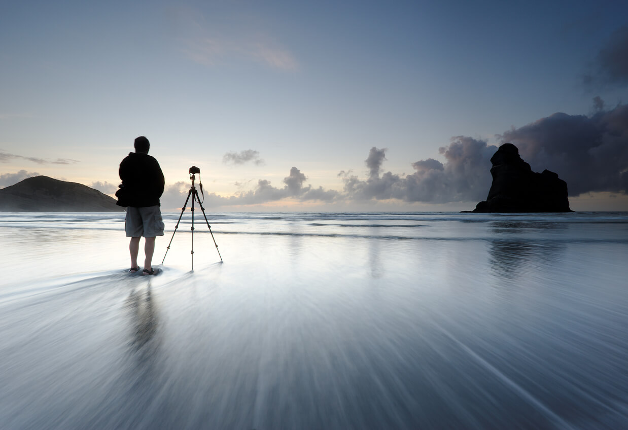 long exposure photography image of a man on a beach with a tripod capturing the waves