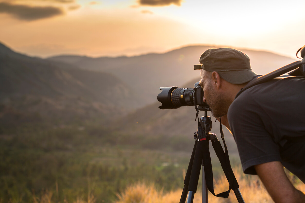 image of a man taking a photograph with a camera on a tripod against a woodland backdrop at sunset