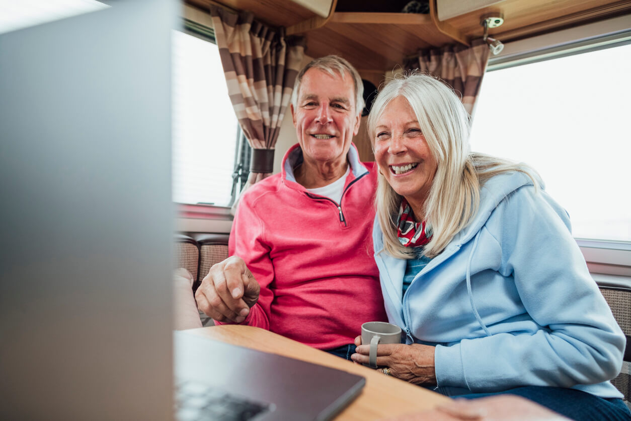 Happy couple speaking to experts over a laptop while in their motorhome