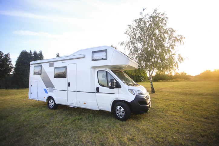 Overcab motorhome outside on grass field with sunlight overlooking the trees