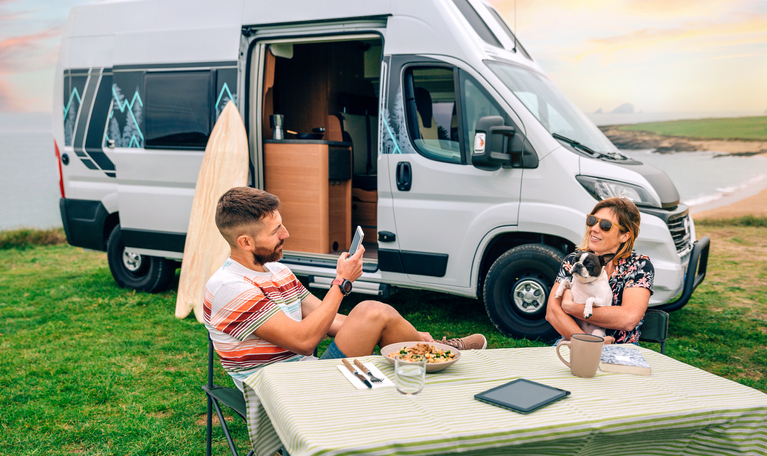 Fixed high-top motorhome with people sat outside at a table with a dog