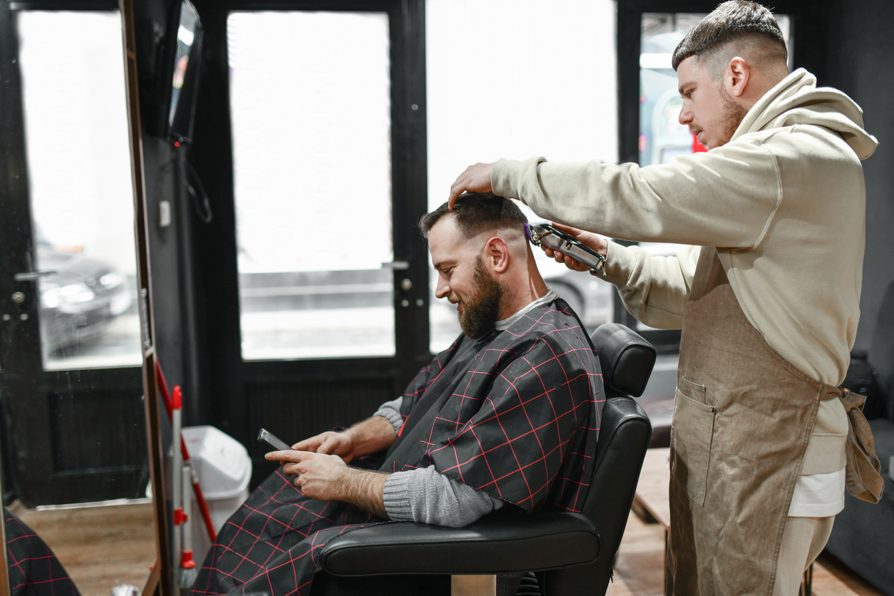 Man sitting in the barbers having his hair cut by male barber with hair clippers